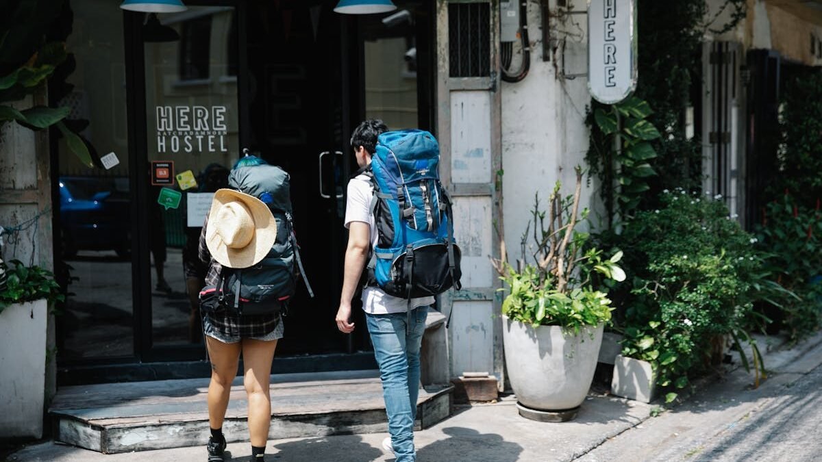 Zwei Rucksacktouristen betreten an einem sonnigen Tag ein Hostel und erkunden das Reisen in der Stadt