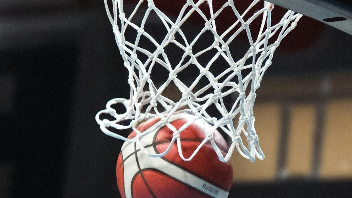 Ein Basketball fliegt mitten in der Aktion durch einen Korb in einer Sporthalle