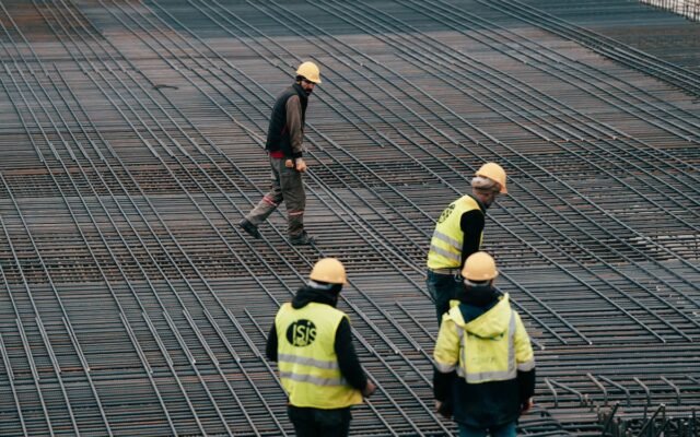 Arbeiter in Schutzkleidung auf einer Baustelle mit Fokus auf Bewehrungsstahl