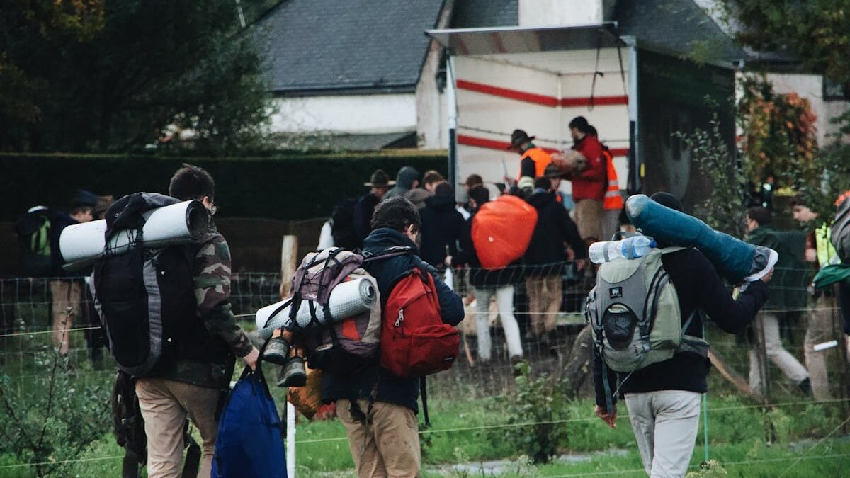Eine Gruppe von Menschen mit Rucksäcken und Campingausrüstung auf dem Weg zu einem Camper-Lkw im Grünen