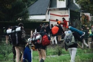 Eine Gruppe von Menschen mit Rucksäcken und Campingausrüstung auf dem Weg zu einem Camper-Lkw im Grünen
