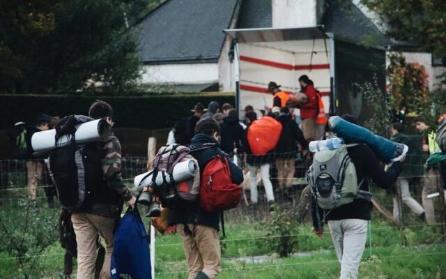 Eine Gruppe von Menschen mit Rucksäcken und Campingausrüstung auf dem Weg zu einem Camper-Lkw im Grünen