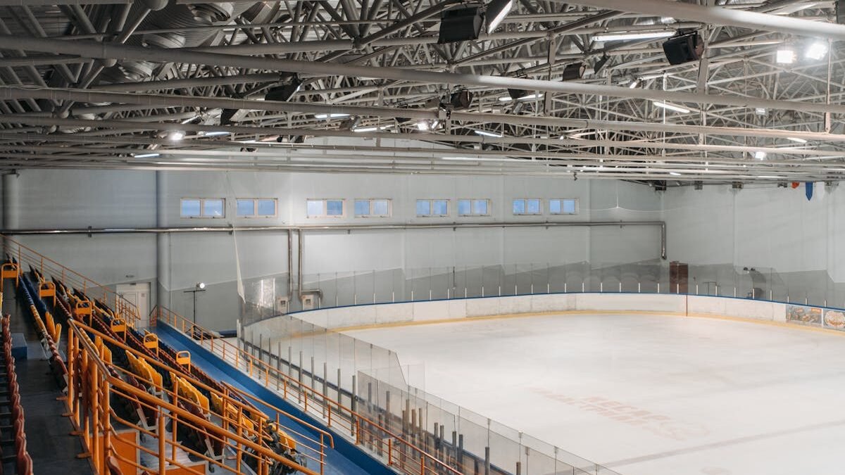 Weitwinkelansicht einer leeren Eishalle mit sichtbaren Stahlträgern und Zuschauerbereich