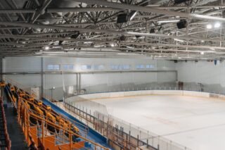 Weitwinkelansicht einer leeren Eishalle mit sichtbaren Stahlträgern und Zuschauerbereich