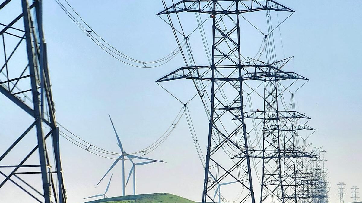 Hochspannungsleitungen und Windkraftanlagen in grünen Feldern