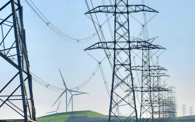Hochspannungsleitungen und Windkraftanlagen in grünen Feldern