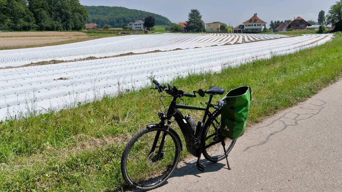Fahrrad geparkt auf einem ländlichen Pfad neben Schweizer Ackerland unter klarem Himmel