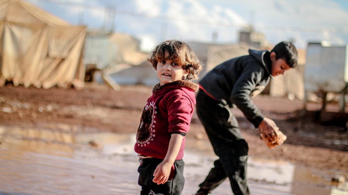 Zwei Kinder spielen in einem schlammigen Bereich eines Flüchtlingslagers