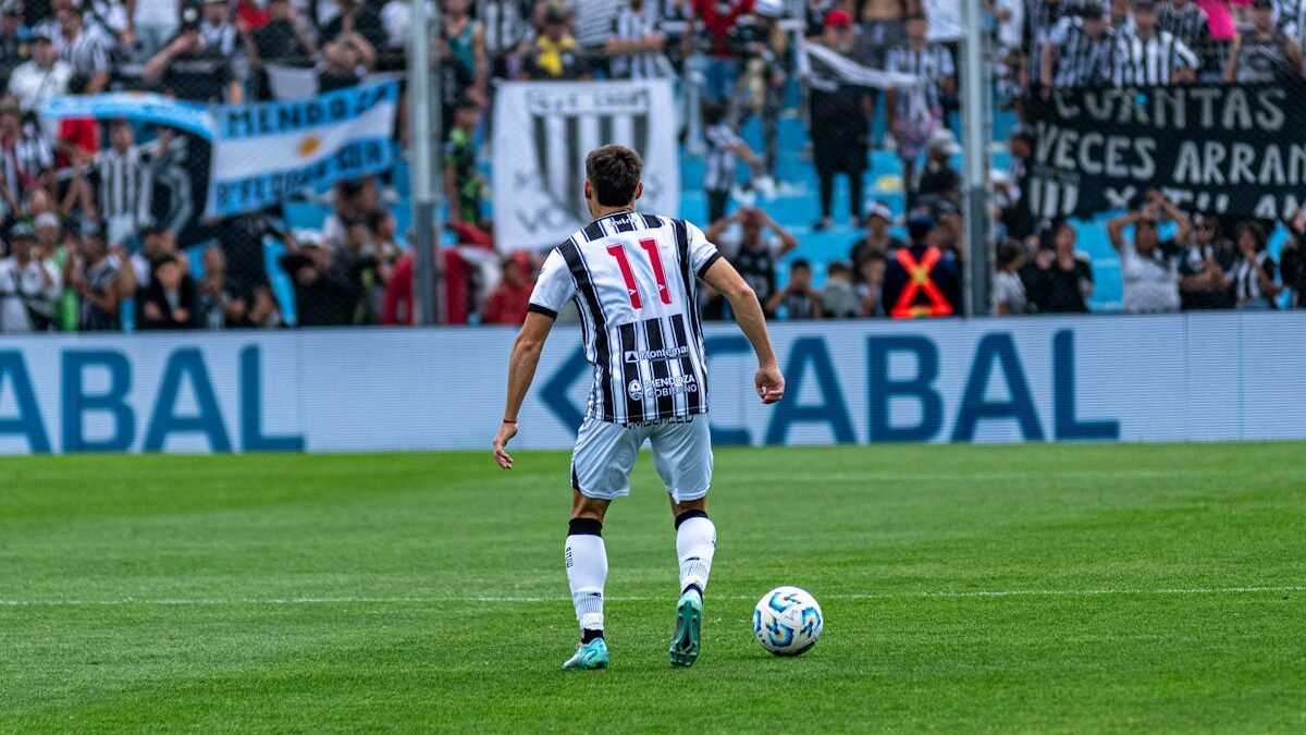 Fußballspieler mit der Nummer 11 in Aktion auf dem Spielfeld während eines Spiels mit jubelnden Fans im Hintergrund