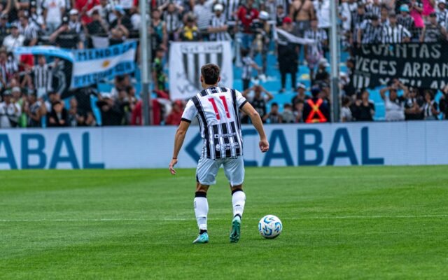 Fußballspieler mit der Nummer 11 in Aktion auf dem Spielfeld während eines Spiels mit jubelnden Fans im Hintergrund