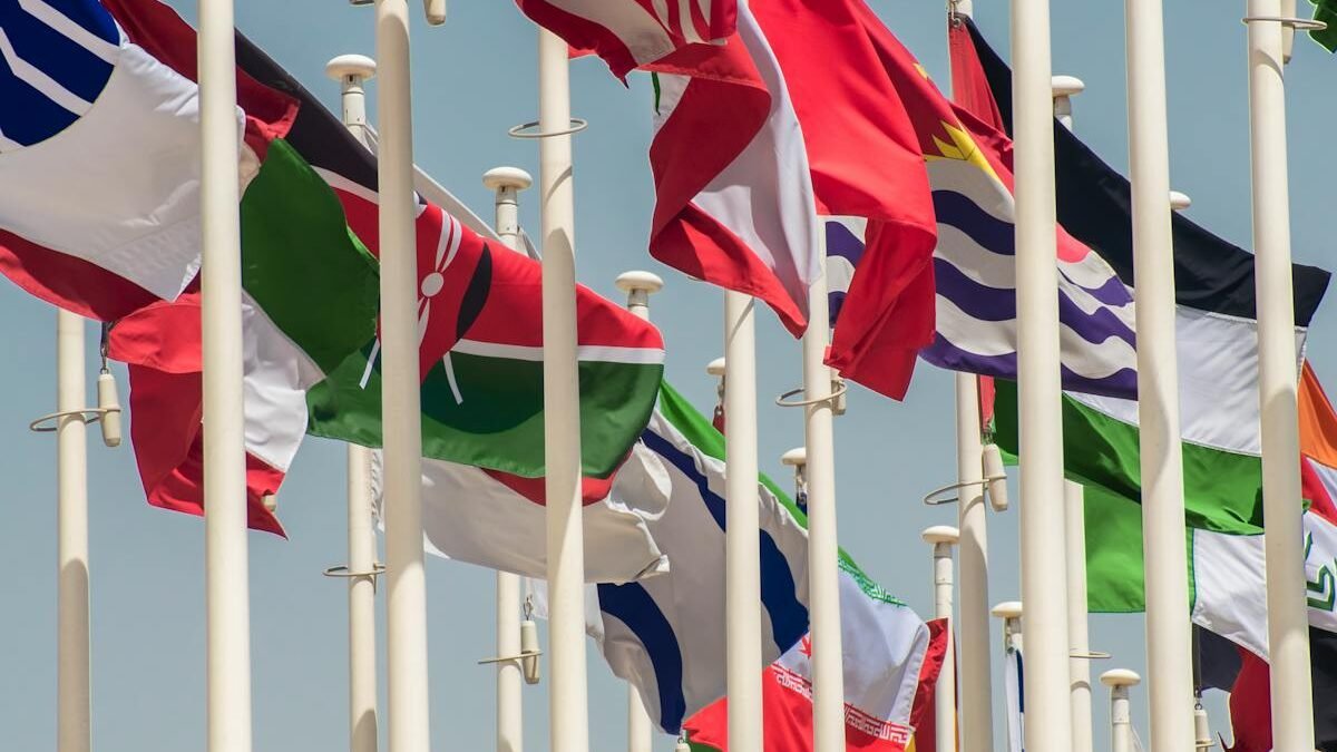 Bunte internationale Flaggen wehen an Fahnenmasten gegen einen klaren blauen Himmel und symbolisieren Einheit und Vielfalt