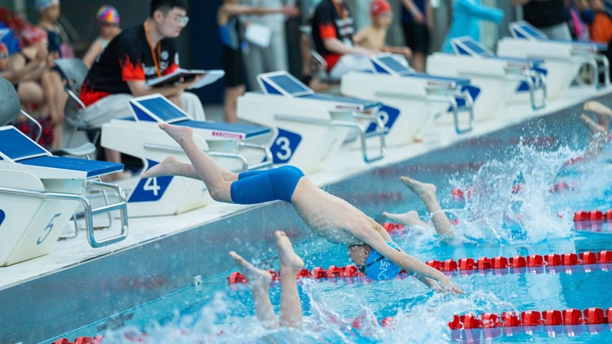 Junge Schwimmer springen zu Beginn eines Wettkampfrennens in einen Pool und zeigen sportliches Können und Teamarbeit