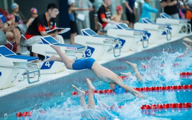 Junge Schwimmer springen zu Beginn eines Wettkampfrennens in einen Pool und zeigen sportliches Können und Teamarbeit