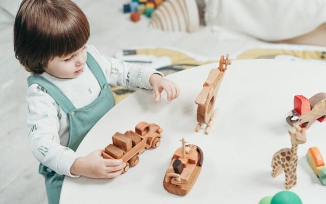 Ein kleines Kind spielt mit Holzspielzeug an einem runden Tisch in einem hellen Spielzimmer