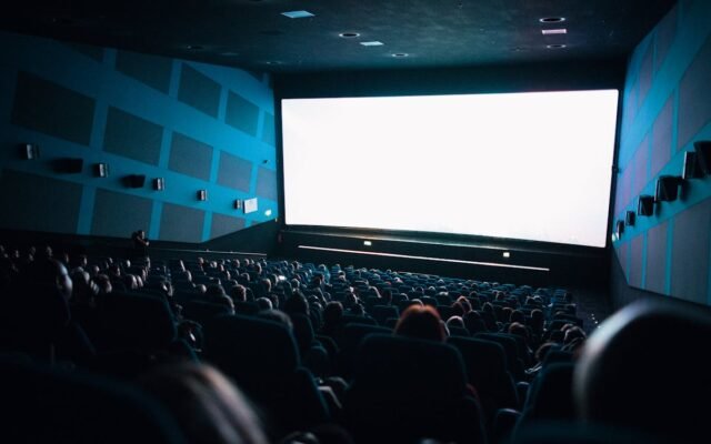 Ein überfülltes Kinopublikum sitzt im Theater und schaut einen Film auf einer großen Leinwand