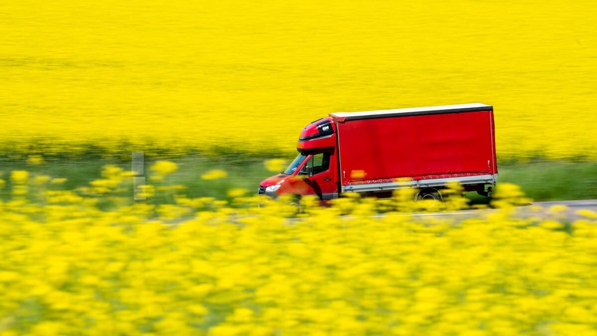 Ein roter Lastwagen fährt durch leuchtend gelbe Senffelder und fängt ländliche Bewegung und Farbkontrast ein