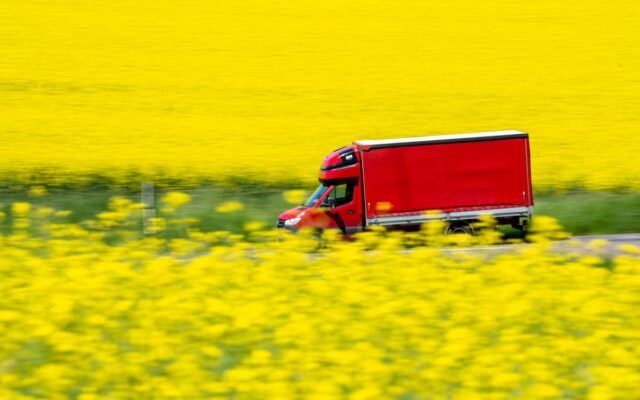 Ein roter Lastwagen fährt durch leuchtend gelbe Senffelder und fängt ländliche Bewegung und Farbkontrast ein
