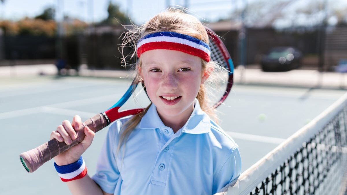 Ein junges Mädchen lächelt mit einem Tennisschläger auf einem Außenplatz