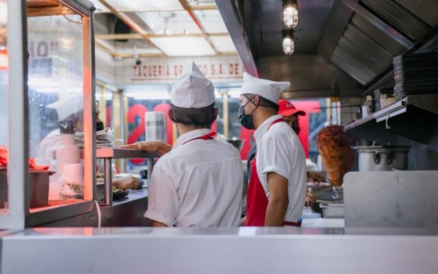 Köche in Uniformen arbeiten in einer offenen Restaurantküche und bereiten Essensbestellungen zu