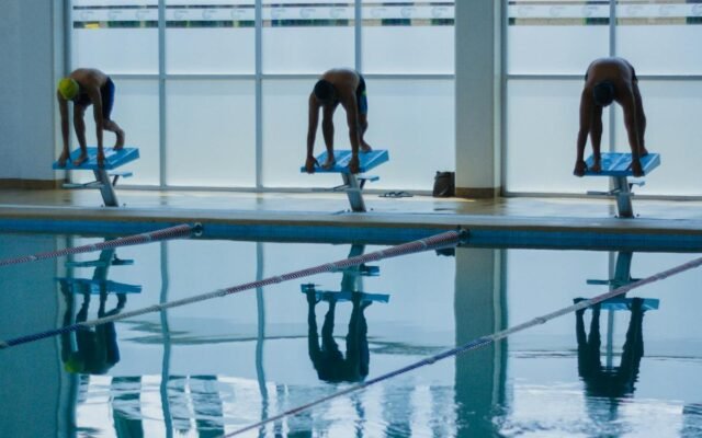 Drei Schwimmer bereit zum Sprung in ein Hallenbad