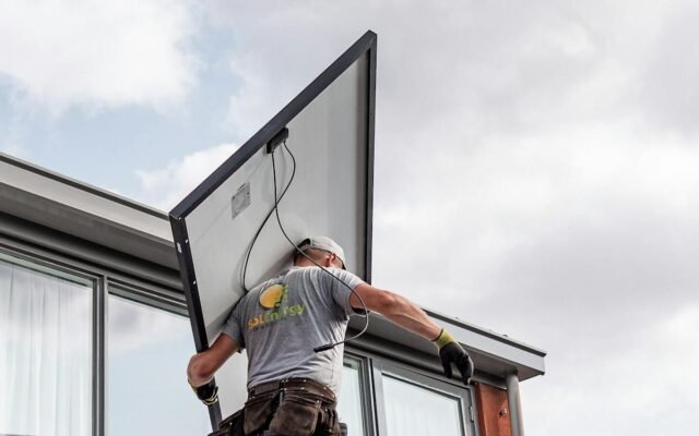 Ein Arbeiter installiert ein Solarpanel auf einem Wohndach und betont erneuerbare Energien
