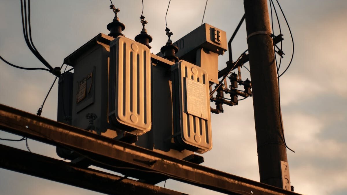 Nahaufnahme eines elektrischen Transformators an einem Strommast vor einem Abendhimmel